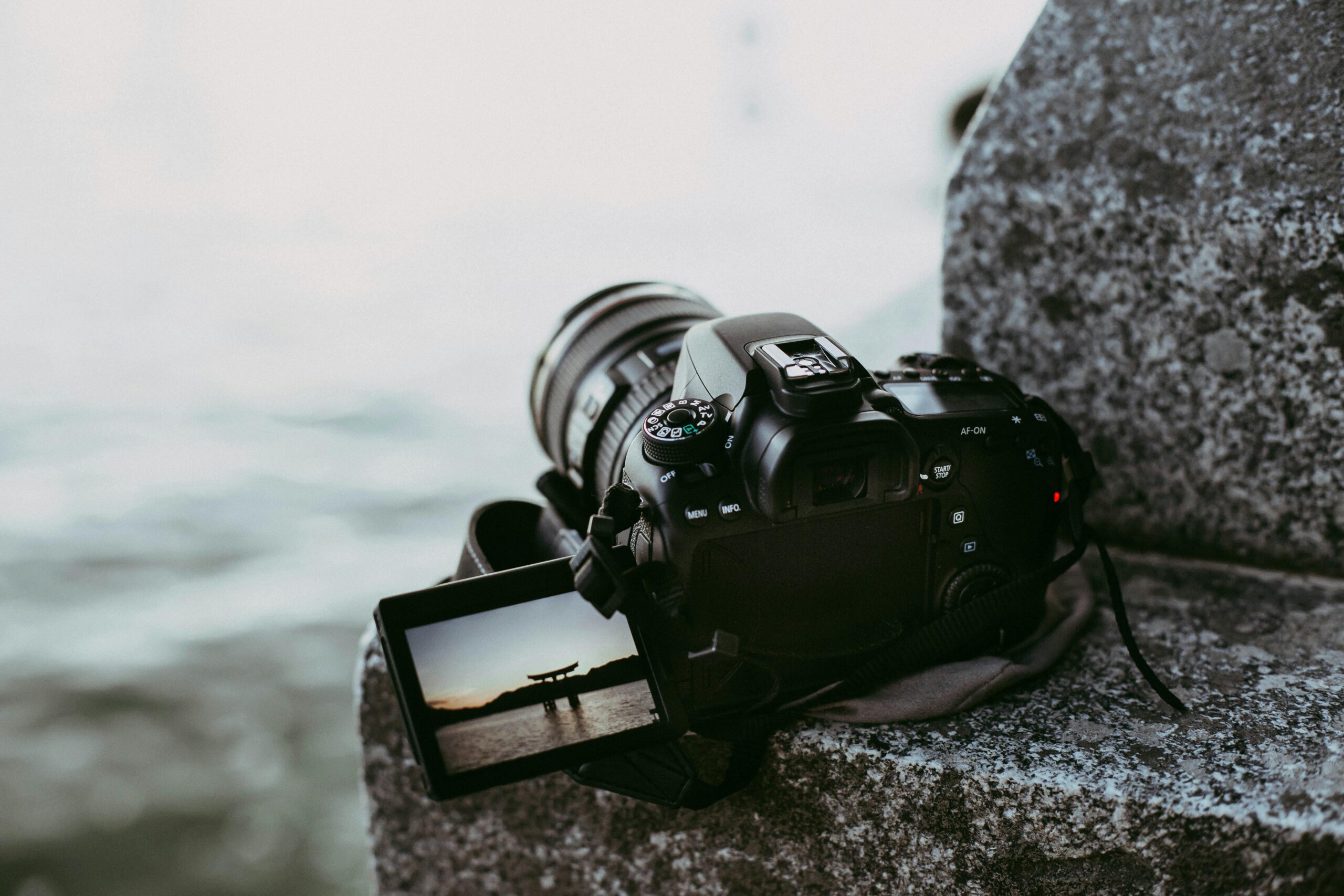 Close-up of a DSLR camera on a rock showing a picturesque landscape on its screen.